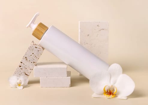 White refillable one pump bottle near white orchid flowers and beige stones on light beige close up, cosmetic mockup. Skincare beauty product package. Natural cosmetics..