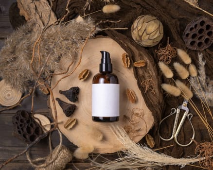 Glass one pump bottle on wood near natural boho decorations top view, label mockup. Skincare beauty product, lotion or essence. Bohemian eco friendly cosmetics flat lay with dried leaves.