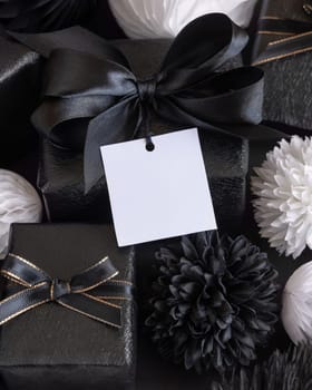 Gift Boxes with Black and white paper flowers and decorations, square gift tag Mockup, copy space. Dark composition with blank label card for Christmas, New Year, Birthday, Anniversary