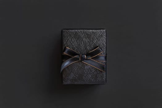 Black Gift Box with a ribbon bow top view on black. Wrapped present for Dark themed Party, Christmas, Birthday, Anniversary. Black Friday concept