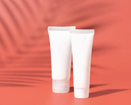 Two white blank plastic tubes on pink close up, palm leaf hard shadows, mockup. Skincare beauty product, body lotion or cream. Natural cosmetics..