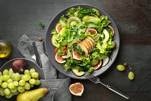 Fresh green leafy salad with fruits and nuts on dark table background. Concept for a tasty and healthy meal