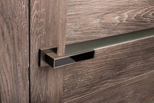 Brown wooden interior door with emphasis on metal handle. Close up of door handle on interior door with frosted glass inserts. Interior details or catalog for furniture store.