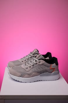 Gray running shoes. Pair of sports shoes standing on white podium on pink background. Side view of gray sneakers on white sole. Sports shoes advertising concept.