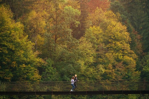 Early morning workout. Young sports family performs a morning jog on a suspension bridge against the backdrop of a mountain forest. Concept of active and healthy lifestyle. Mountain forest landscape.