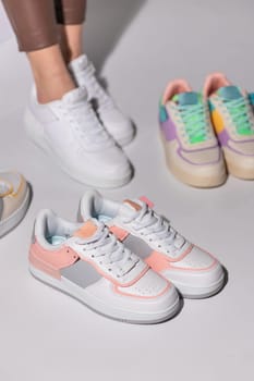 Close up of stylish white and pink women's sneakers on background of other sports shoes. Woman on white background trying on different types of sneakers. Seasonal sales, promotions, discounts on shoes