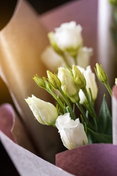 Close up of white eustoma flowers in a bouquet wrapped in pink paper. Concept of congratulations on International Women's Day, Birthday and Mother's Day.