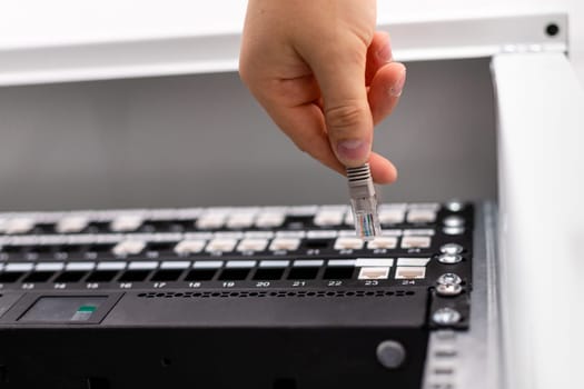 Man works with telecommunications. IT consultant connects network cable into switch in datacenter. Bottom view close up of male technician hand switching internet cable of powerful routers.
