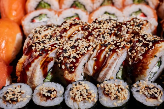 Close up of sushi rolls with tuna, eel, cheese, cucumber and avocado drizzled with sauce and sprinkled with sesame seeds. Japanese food concept.