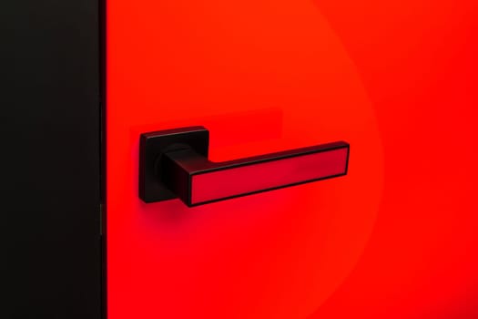 Close up of stylish matte black and red door handle on colored interior door. Handle with insert of same color as door. Bright red door for home or office. Interior details concept.