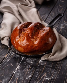 Close up of fragrant baked homemade bread on dark wooden table. Fragrant round bread with brown crust lies on frying pan near gray cloth. Concept of bakery products.