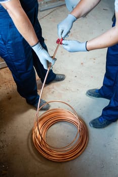Installation works. Two men in blue overalls and protective gloves prepare underfloor heating for water heating on construction site. Construction work concept.