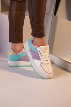 Close up of fashionable colored sneakers on the legs of a teenage girl. Girl in brown pants stands by mirror showing off a new collection of laceup sports shoes.