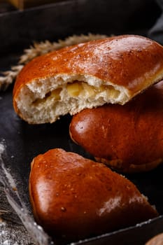 Close up of homemade buns with slices of apples inside on dark background. One broken bun in which the filling is visible lies on another bun. Concept of homemade sweet pastries and fruit fillings.