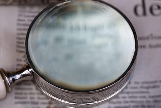 A magnifying glass, a reading aid lies on an old newspaper.
