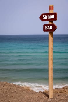 On one coast there is a sign with the indication to the beach and the indication to the bar.