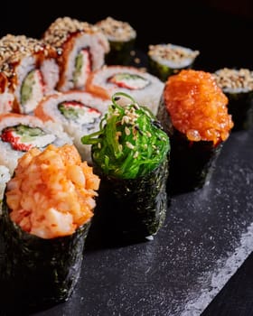 Close up of delicious sushi set with rolls of California, sashimi and maki on a black plate. Japanese oriental food with raw fish, cheese, sesame seeds, caviar and seaweed. Selective focus.