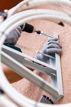 Process of installing air conditioning on street. Close up of male worker installing wall mount for outdoor air conditioner unit. Man with drill tightens screws to install air conditioner in wall.