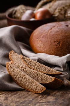 Country still life. Sliced pieces of fresh rye black bread on lies on burlap on old wooden table. Close up of appetizing pieces of bread on background of round homemade freshly baked bread.