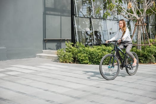Asian beautiful young businesswoman with helmet riding bicycle go to office work at city street with bicycle in morning, Happy lifestyle woman bike after business work outside building , Eco friendly