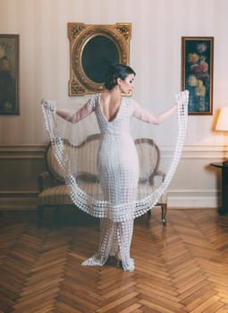 Stylish woman with hairstyle and makeup in elegant laced white dress for special occasions. Beautiful bride posing in designer wedding dress in classical luxury interior.