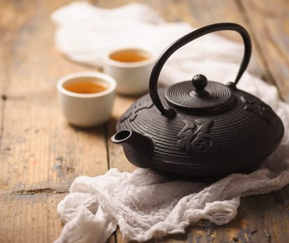 Still life with traditional asian herbal green tea prepared in vintage cast iron teapot with organic dry herbs on rustic wooden table.