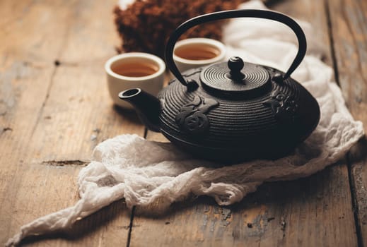 Still life with traditional asian herbal tea prepared in vintage cast iron teapot with organic dry herbs on rustic wooden table. Retro filter.