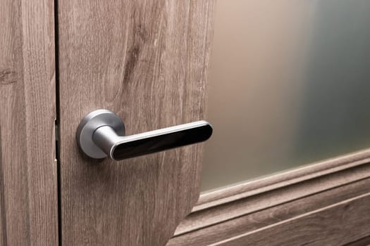 Close up of steel door handle on brown wooden door. Dark oak door with frosted glass. Concept of interior details and the choice of interior doors during the repair.