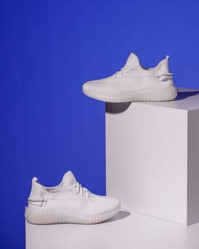 Fashion shoes. Pair of stylish fashionable white women's sneakers standing on white catwalk on blue background. Place for text. Advertising banner.