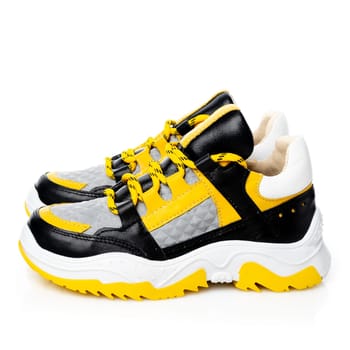 Close up of stylish trendy children's sneakers isolated on white background. Side view of bright sneakers in white, black and yellow. Seasonal sales, promotions, discounts on shoes.