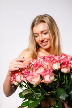Close up of bouquet of roses on background of young sexy and sensual women. Naked blonde woman with large bouquet of pink roses on white background. Advertising banner. Feminine concept.