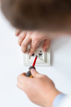 Installing socket close up. Electrician hands tighten bolts in wall fixture or socket using screwdriver. Electrician performs electrical work at home during repairs. Renovation process.