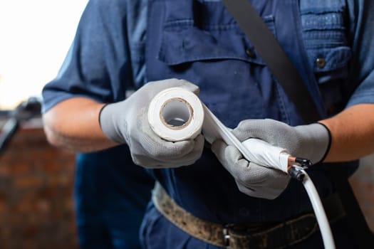 Professional workers in gloves and overalls will prepare pipes when installing heating system in empty apartment. Close up of men winding pipes and cables with insulating tape.