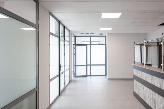 Stylish minimalist office corridor with empty receptions in modern coworking center. Interior of bright corridor with large matte plastic doors and windows. Reception is enclosed by glass damper.