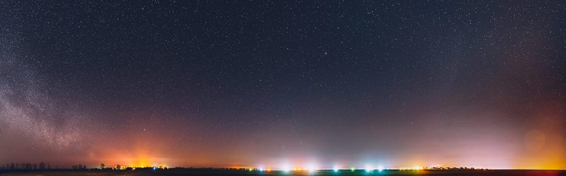 Night Starry Sky With Glowing Stars Above Countryside Landscape. Milky Way Galaxy And Rural Field Meadow In Early Spring. Panorama, Panoramic View.
