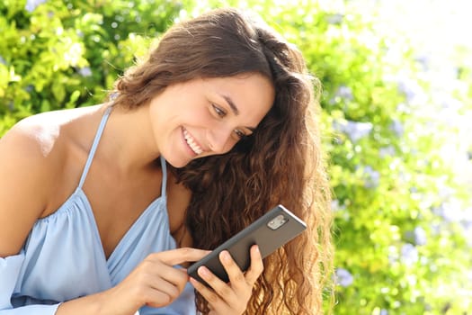 Happy woman in a green garden using smart phone