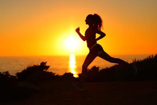 Side view backlight portrait of a silhouette of a runner running at sunset on the beach