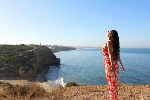 Woman in red dress breathing fresh air on a clif on the beach