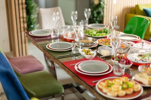 Beautifully catering table set service with variety of dishes to celebrate in restaurant. Colored chairs in bright modern cafe or restaurant at table with utensils, wine glasses and snacks.