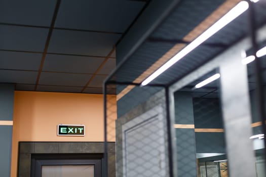 Exit sign in Ukrainian and English hangs above door in public place such as gym, swimming pool or fitness club. Board with inscription which is illuminated by green led light.