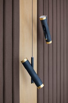 Close up of two small minimalist modern pendant lights in room in new home. Black and gold original modern loft pendant lights hang on different levels against background of classic brown curtains.