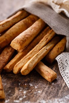 Bread snack. Traditional homemade baked snack in form of long bread sticks. Close up of fresh bread sticks lying in burlap sack on ancient rustic wooden board. Selective focus.