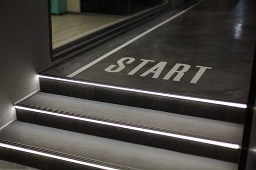 Staircase in building. Close up of dark staircase with LED backlight and with inscription Start. Selective focus detail in new building such as concrete steps with white LED illumination