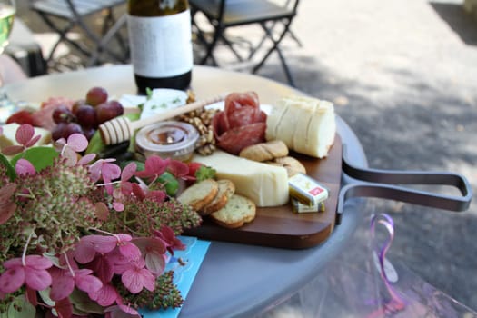 Grazing board with assorted cheeses, meats, crackers, wne and bouquet of flowers for outdoor dining