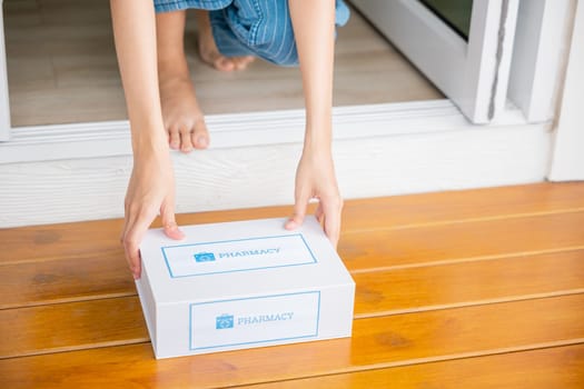 Close up hands of sick Asian woman sitting at door to receive medication first aid pharmacy box from hospital delivery service at floor home, merchandise medicine online business, healthcare concept