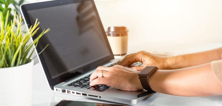 Web application development. programmer woman writing program code sitting at workplace in office, software developer hands coding HTML programming with laptop computer, IT start up concept, back view
