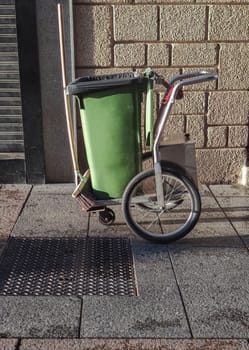 Street sweeper cart with green dumpster and sweep. Downtown background