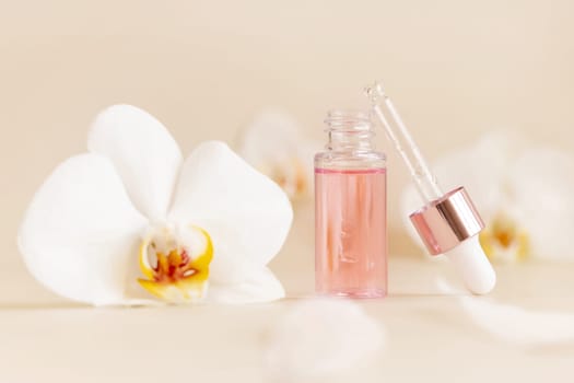 Light Pink opened Dropper Bottle with serum and a pipette cap near white orchid flowers on light beige, close up, copy space. Skincare cosmetic product, essence or serum. Everyday beauty routine.