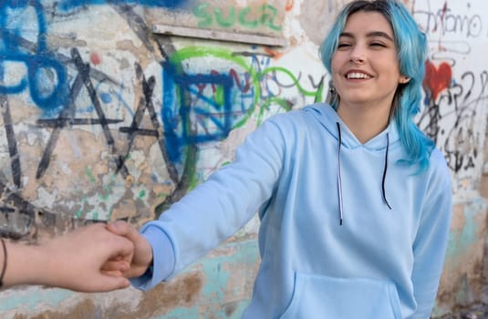 Teenager girls holding hands and laughing. Blue haired young woman wearing hoodie spending time with friends outdoor near graffiti wall. Clothing mockup.