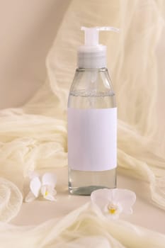 One pump bottle filled with liquid near orchid flowers and tulle on light beige close up. Packaging Mockup. Exotic natural cosmetics, romantic composition, everyday skincare routine..